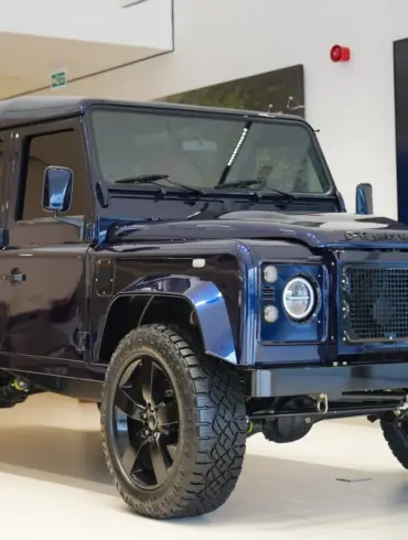 Land Rover Defender 110 300 TDI von 1999 in Tanzanite Blue, modernisiert mit LED-Leuchten und großen 20-Zoll-Rädern, ausgestellt in einem Showroom.