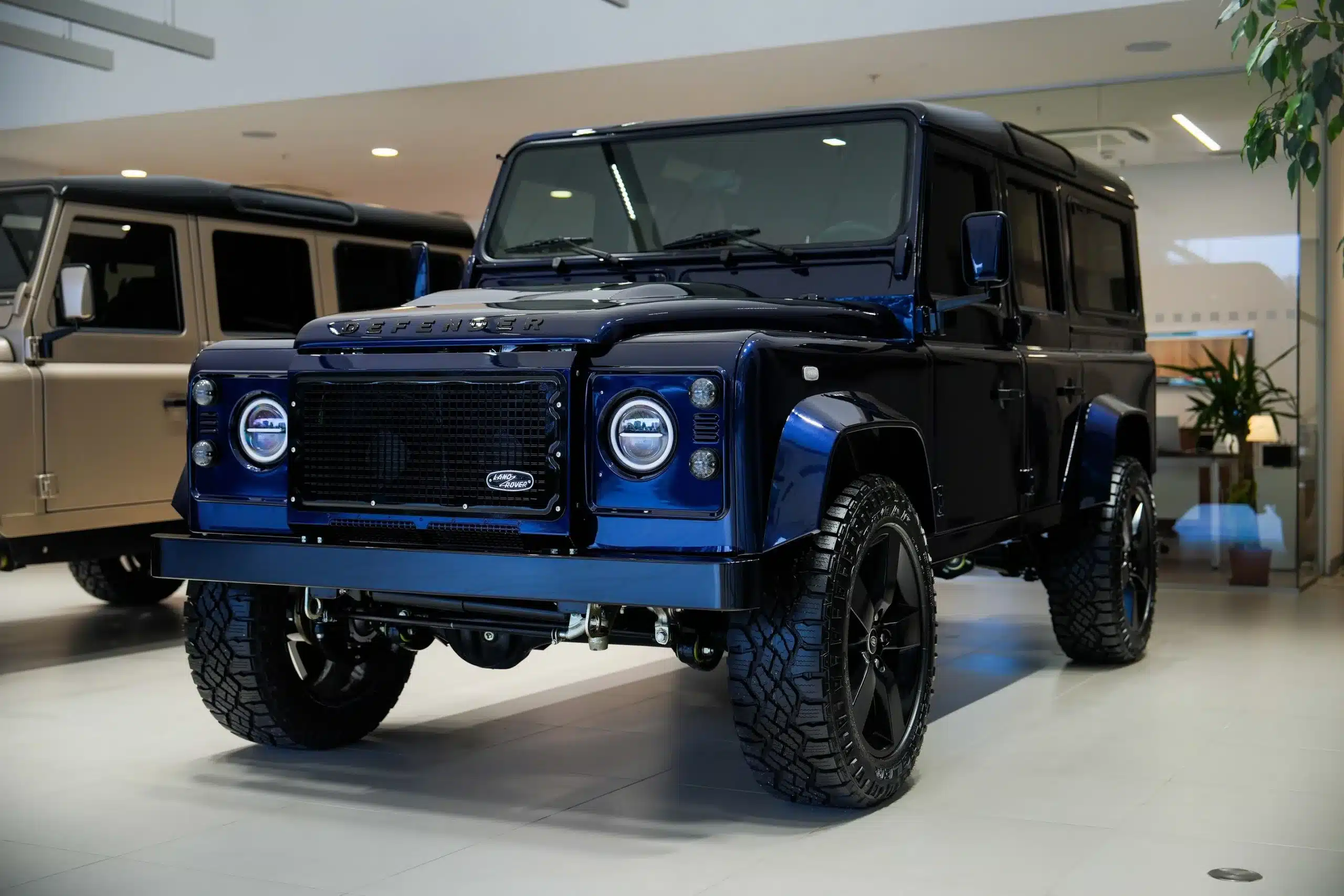Land Rover Defender 110 aus dem Jahr 1999 mit 300 TDI Dieselmotor in blauer Sonderlackierung, stehend in einer modernen Ausstellungshalle.