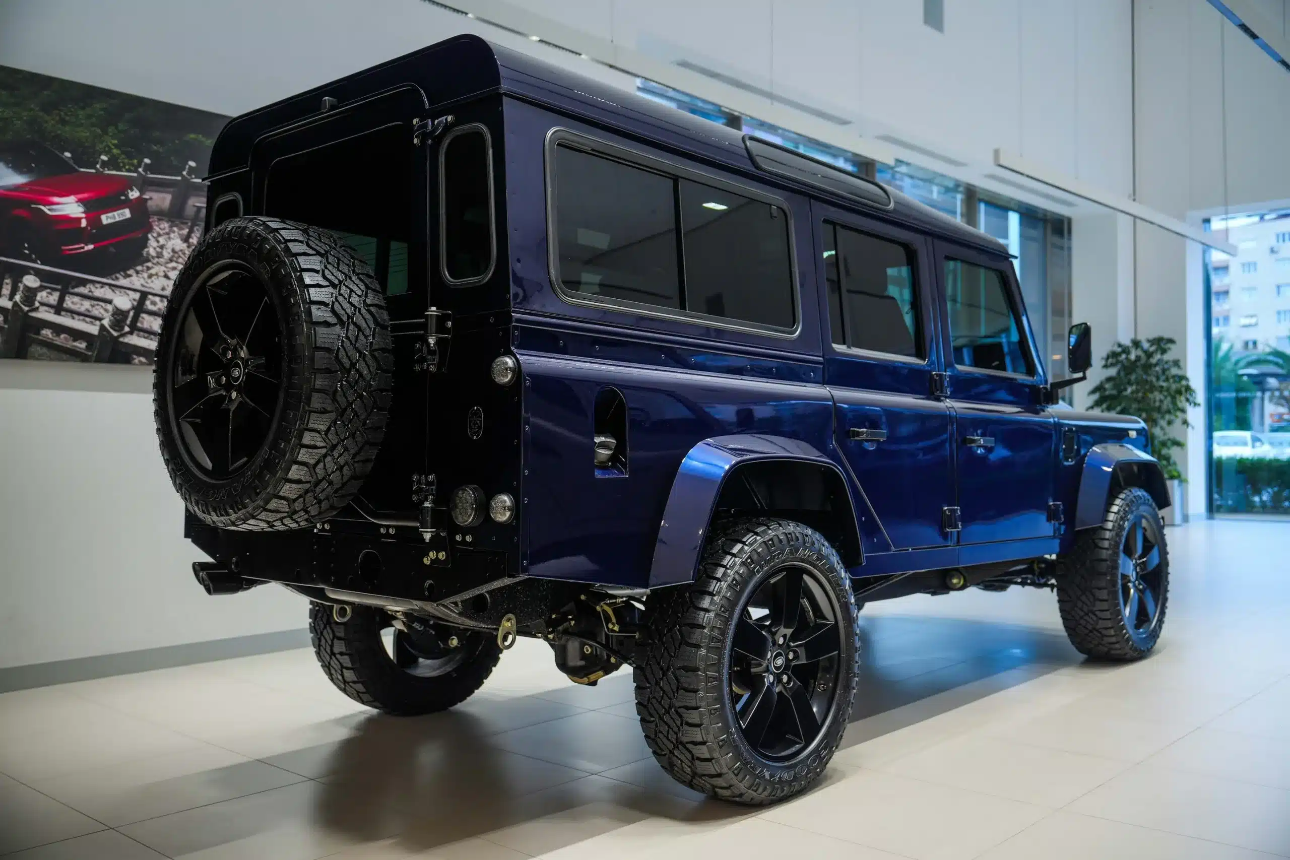Land Rover Defender 110 300 TDI von 1999 in Tanzanite Blue, restauriert mit schwarzen Offroad-Felgen, Ersatzrad und modernen Ausstattungsmerkmalen, ausgestellt im Showroom.