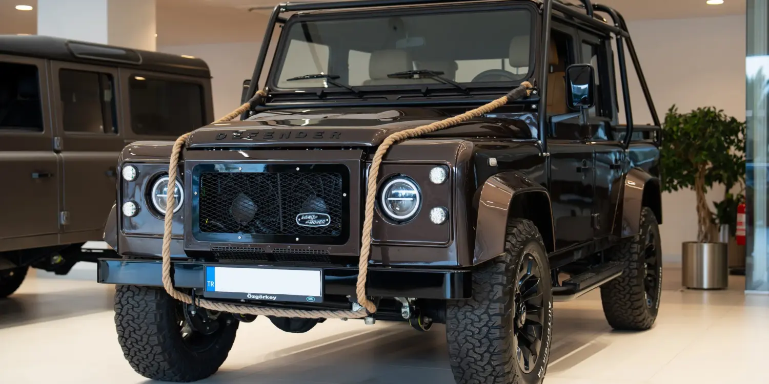 Brauner Land Rover Defender 110, 1999, mit Seil an der Front im Innenraum eines Autohauses