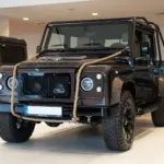 Brauner Land Rover Defender 110, 1999, mit Seil an der Front im Innenraum eines Autohauses