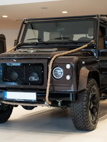 Brauner Land Rover Defender 110, 1999, mit Seil an der Front im Innenraum eines Autohauses