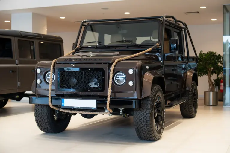 Brauner Land Rover Defender 110, 1999, mit Seil an der Front im Innenraum eines Autohauses