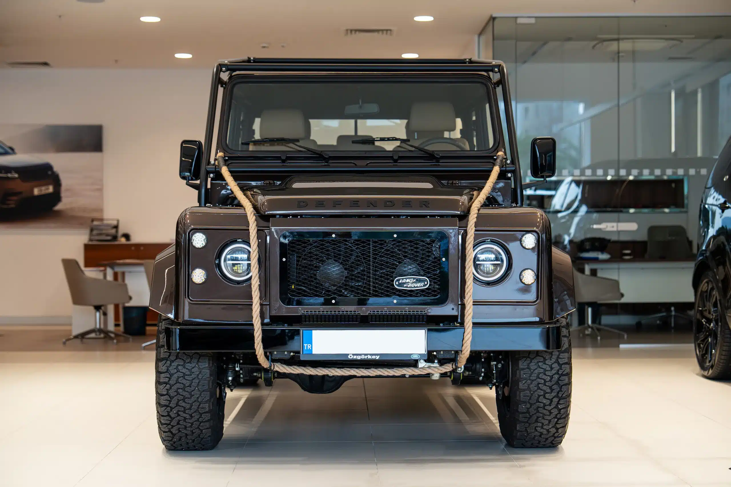 Brauner Land Rover Defender 110, Modelljahr 1999, Frontansicht mit Offroad-Details im Showroom
