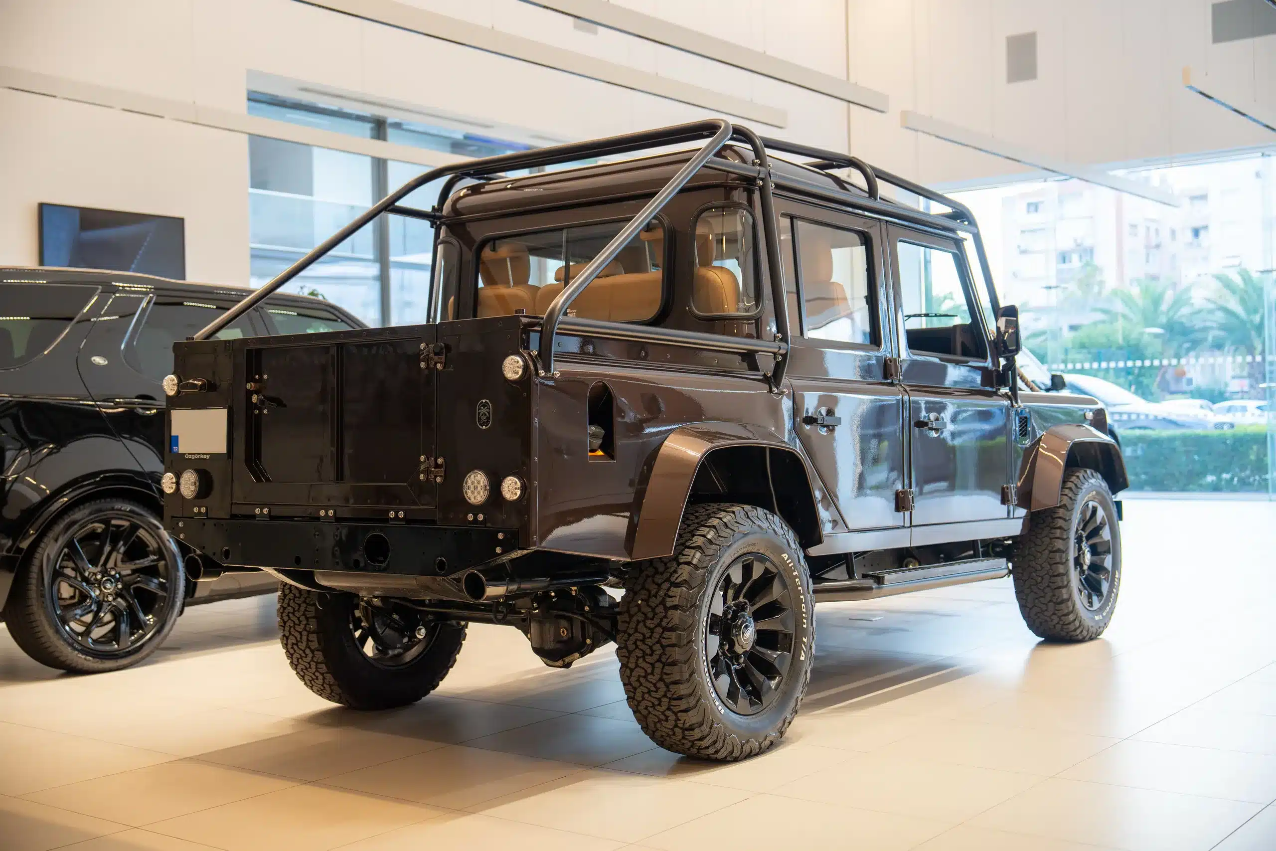 Brauner Land Rover Defender 110, Modelljahr 1999, mit Geländebereifung und Überrollbügel im Ausstellungsraum.