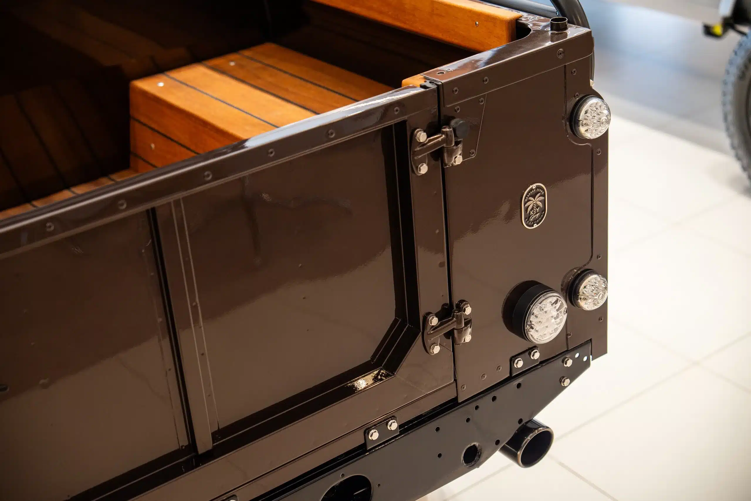 Heckansicht eines braunen Land Rover Defender 110 von 1999 mit geöffneter Klappe und Holzladeraum.