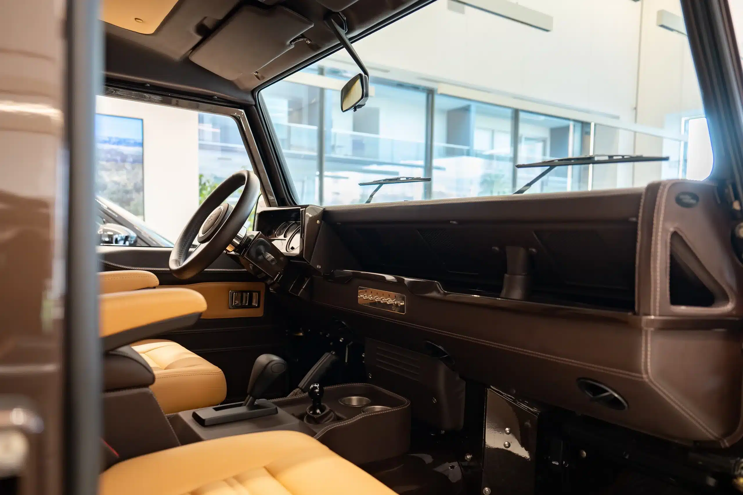 Innenraum eines Land Rover Defender 110, Baujahr 1999, mit braunem Armaturenbrett und beigen Ledersitzen