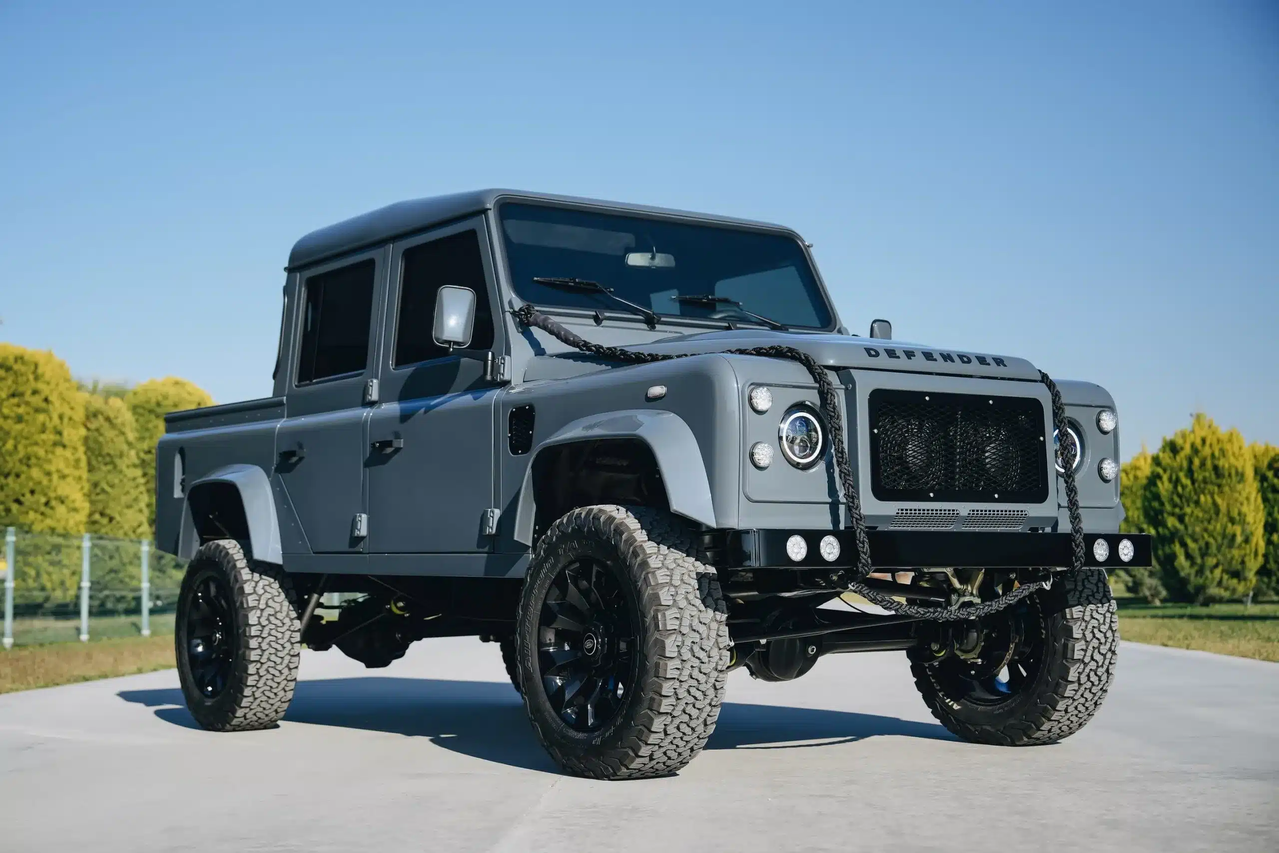 Land Rover Defender 110 als Pick-up mit Offroad-Umbau und Seilwinde, geparkt im Freien.