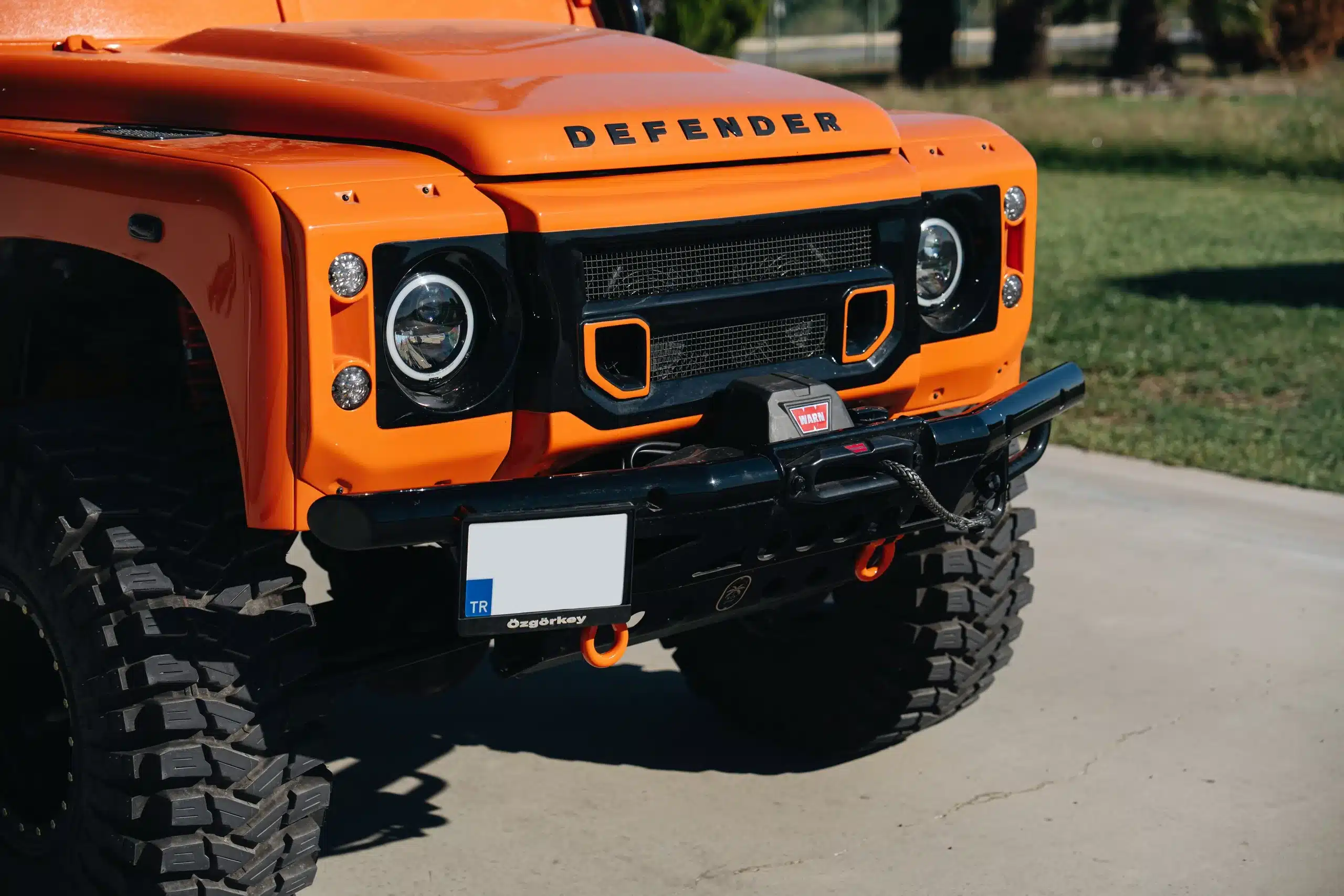 Frontpartie eines orangen Land Rover Defender 110 aus dem Jahr 1991 mit Seilwinde und Offroad-Reifen