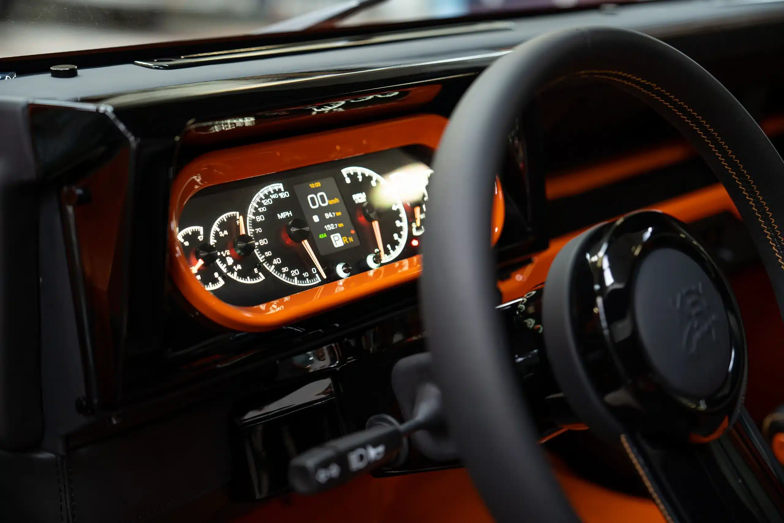 Modernisiertes Armaturenbrett eines orangen 1991er Land Rover Defender 110 mit digitalen Anzeigen und Lenkrad