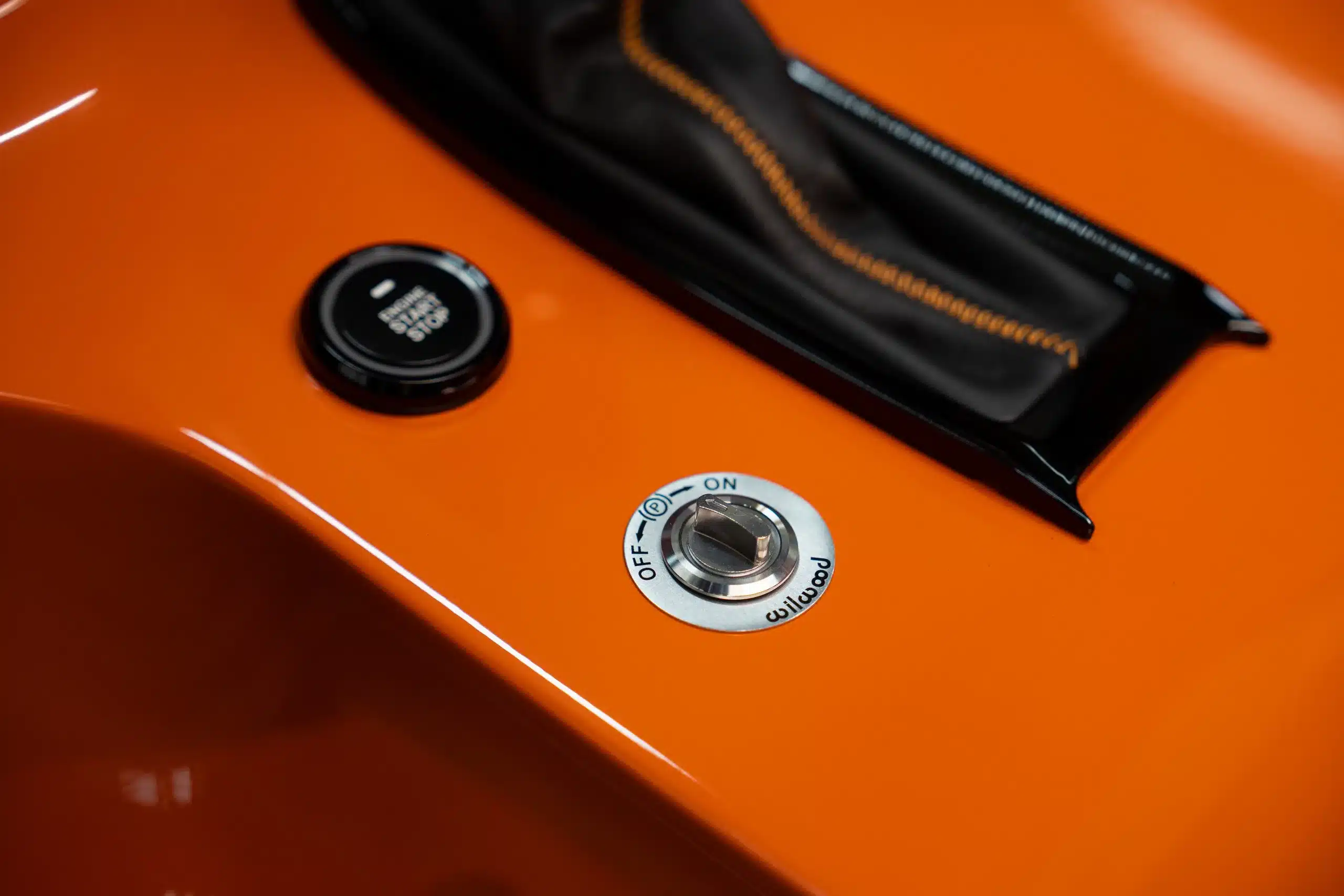 Detailaufnahme Start-Stopp-Knopf und Wilwood-Handbremshebel auf orangefarbener Mittelkonsole eines Land Rover Defender 110 von 1991