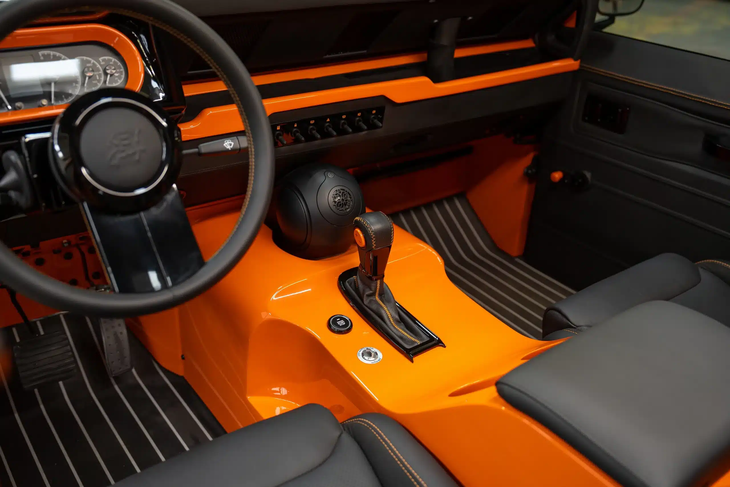 Innenansicht des orangefarbenen 1991er Land Rover Defender 110 mit Lenkrad und Schalthebel.