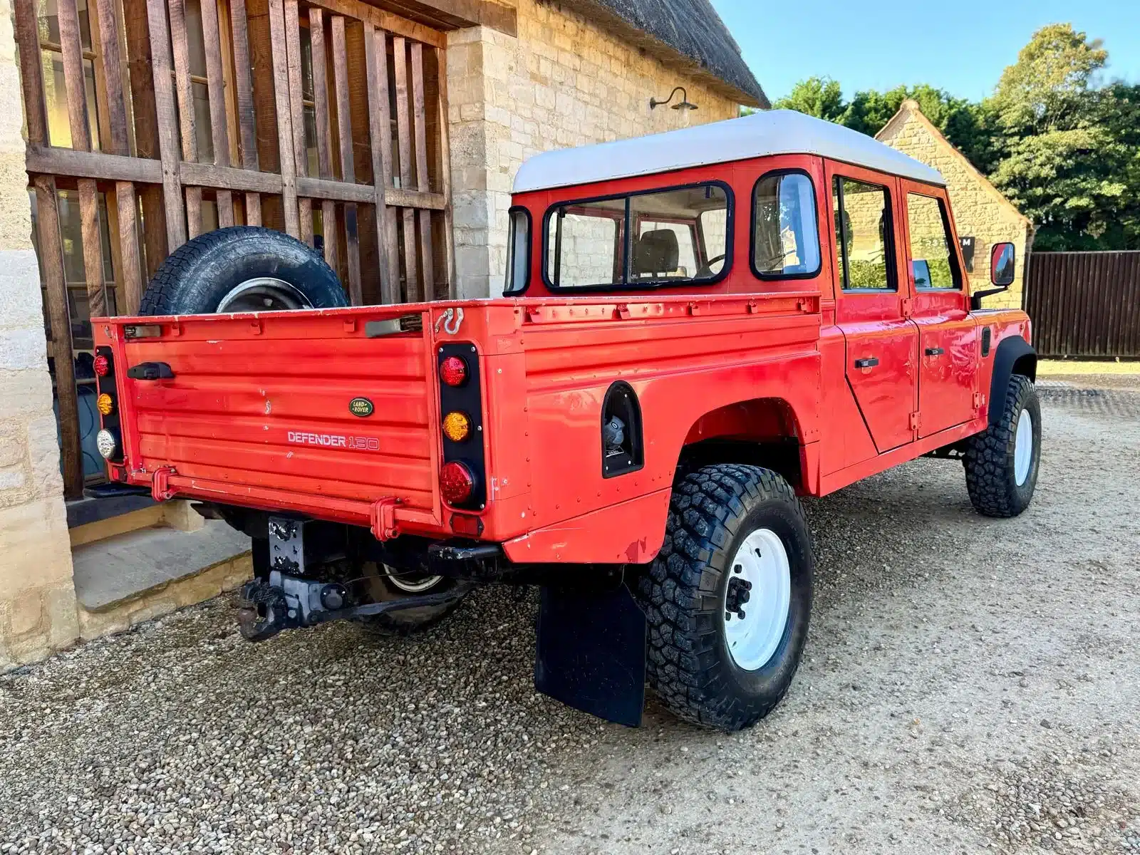 Land Rover Defender 130 300Tdi Doppelkabine von 1995 in Masai Red mit weißem Dach, auf einem Hof geparkt.