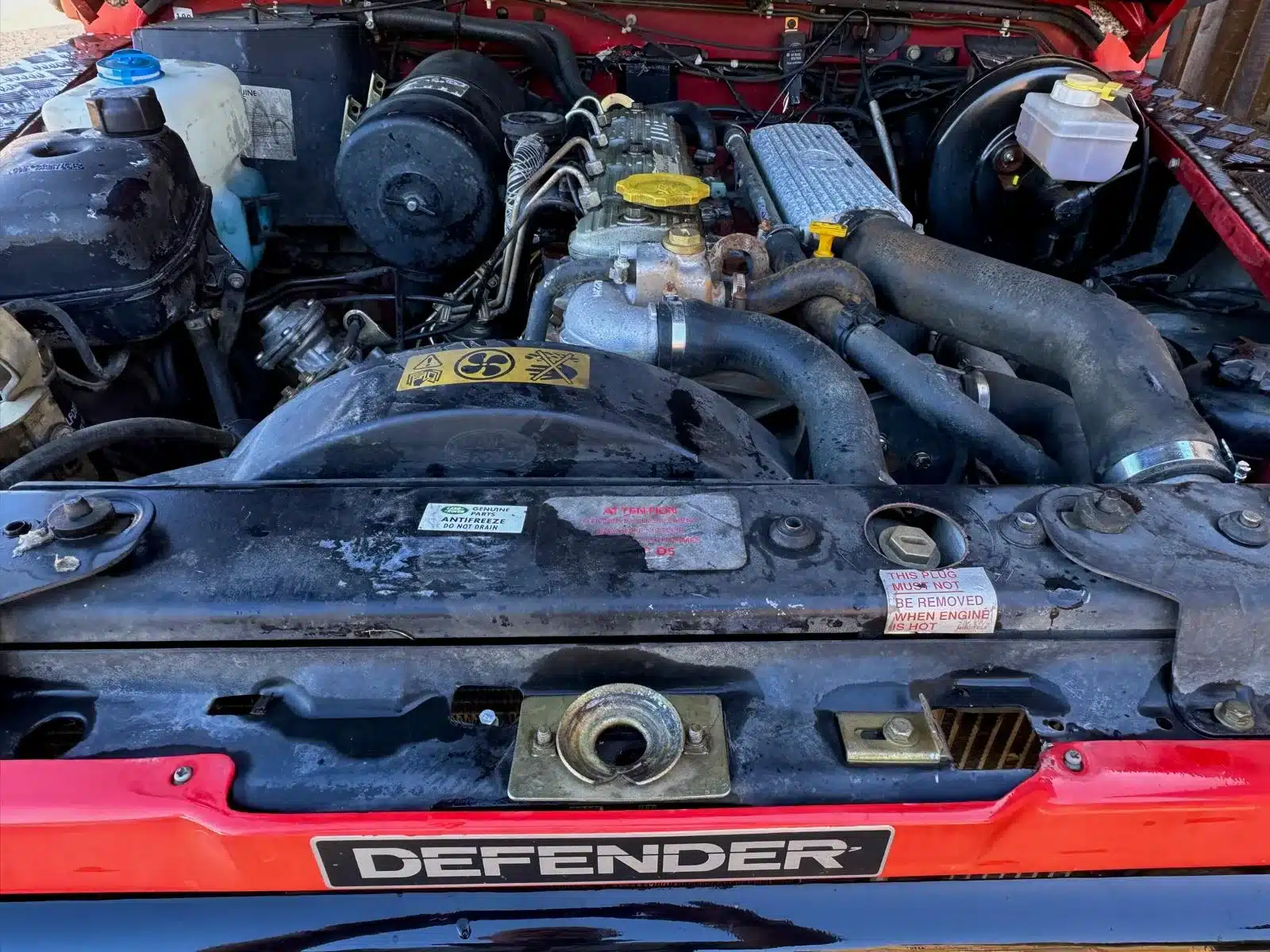 Motorraum eines Land Rover Defender 130 300Tdi von 1995, gut erkennbar mit originalen Komponenten und Gebrauchsspuren.