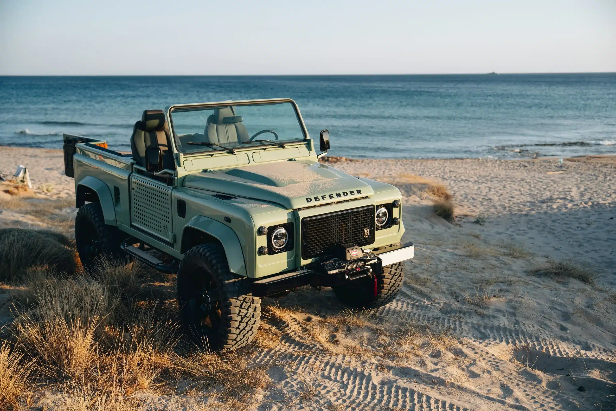 Land Rover Defender 90 in Grasmere Green, Baujahr 1995, als Cabrio-Variante am Strand mit Blick auf das Meer