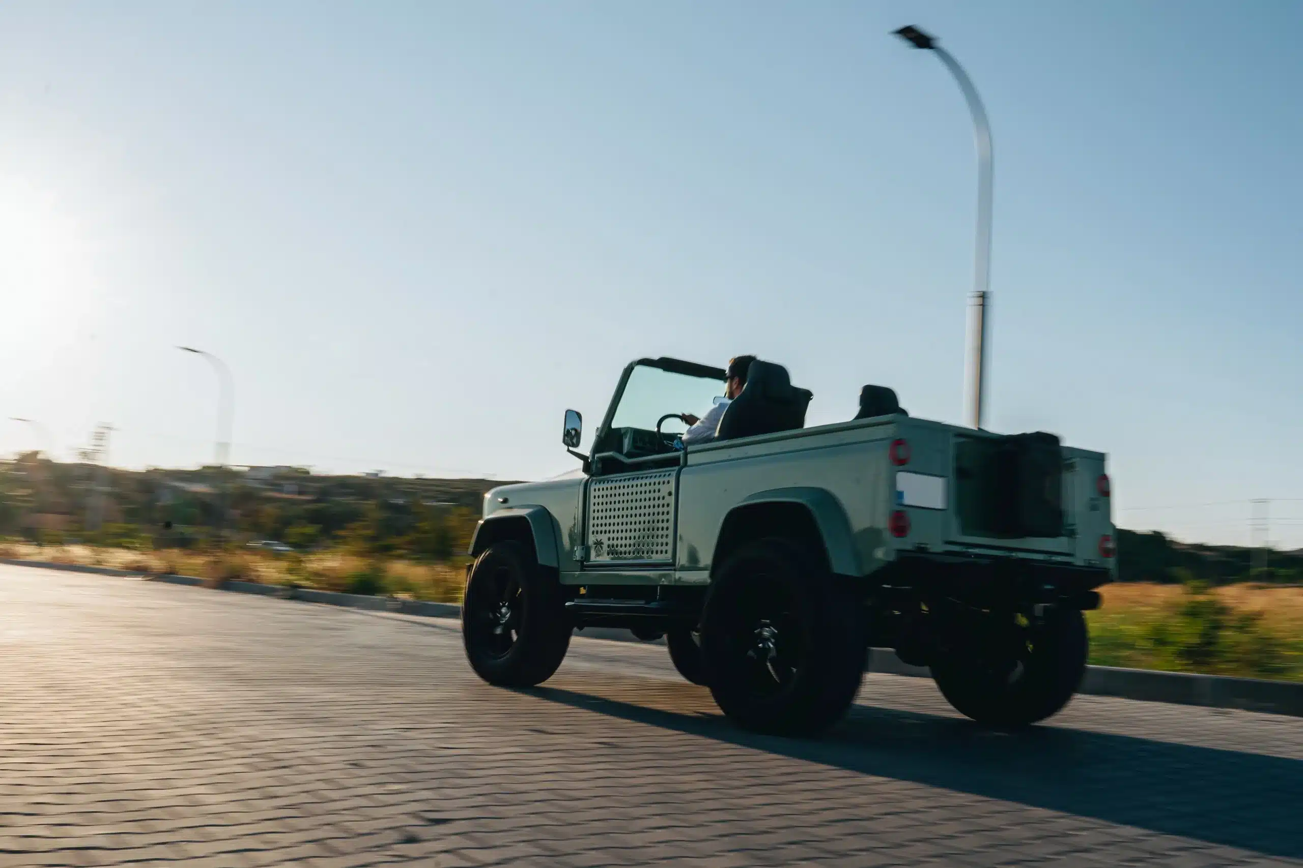 Land Rover Defender 90 Cabrio, Baujahr 1995, in Grasmere Green, während der Fahrt auf einer sonnigen Landstraße.