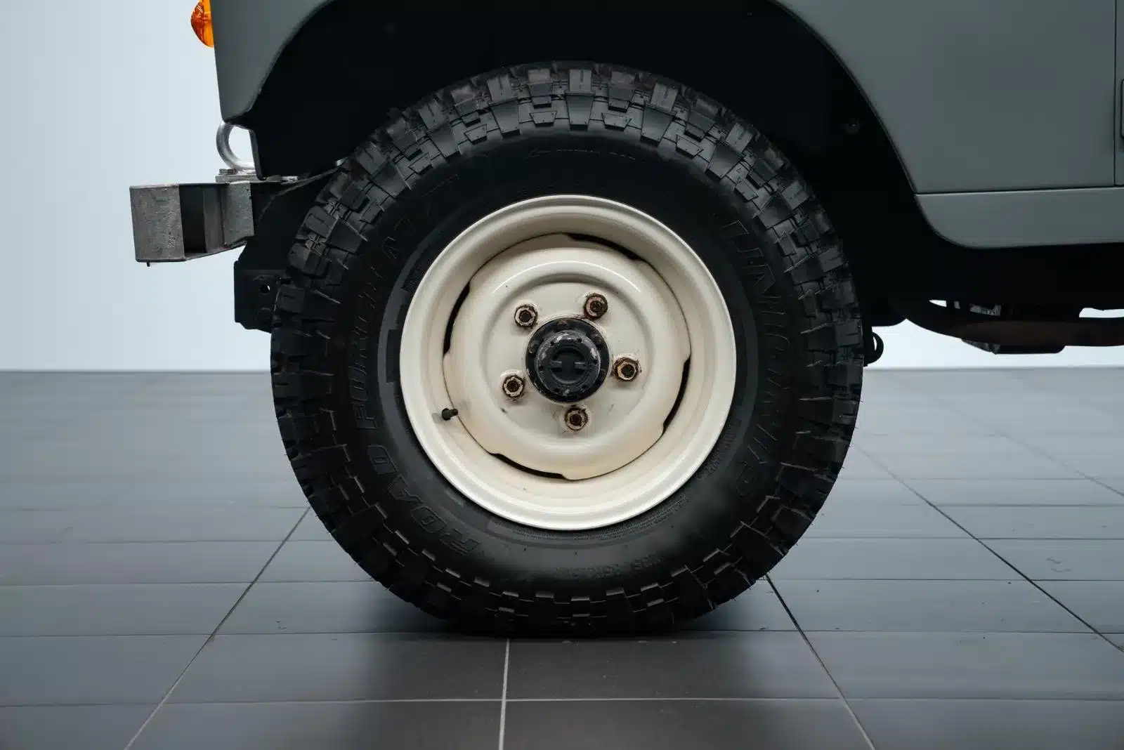 Nahaufnahme eines grobstolligen Reifens mit klassischer Felge am Land Rover Serie III 109 LWB Militärumbau