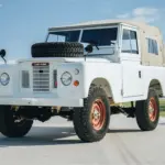 Frontansicht eines Land Rover Series III von 1973 in weiß mit Ersatzrad auf der Motorhaube und beigem Verdeck
