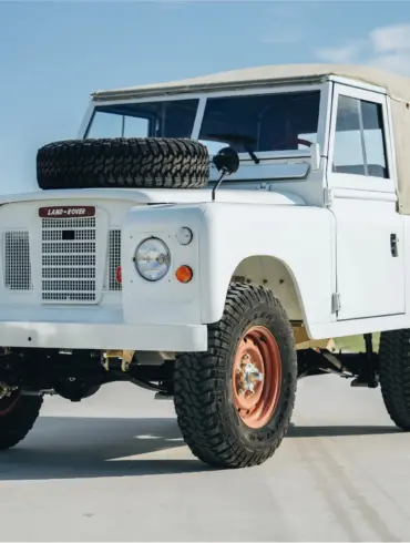 Frontansicht eines Land Rover Series III von 1973 in weiß mit Ersatzrad auf der Motorhaube und beigem Verdeck