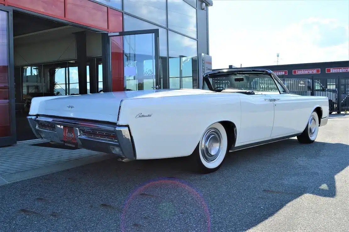 Lincoln Continental 4-door Convertible von 1967 in Weiß mit offenem Verdeck, Rückansicht, vor einem Showroom geparkt.