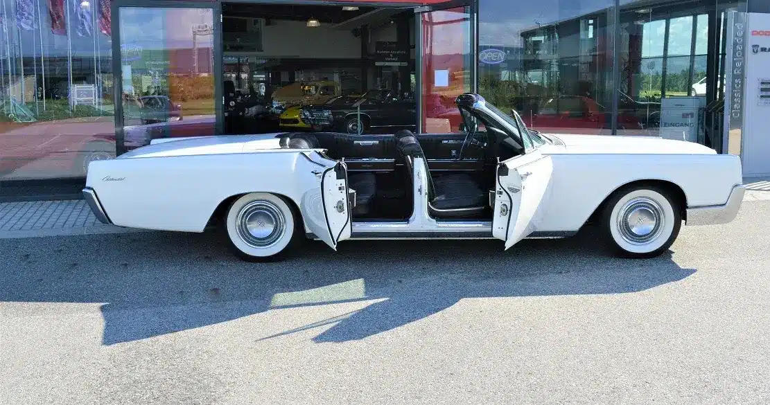 Lincoln Continental 4-Türer Cabriolet von 1967 in Weiß mit geöffneten Türen vor einem Autohaus.
