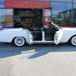 Lincoln Continental 4-Türer Cabriolet von 1967 in Weiß mit geöffneten Türen vor einem Autohaus.