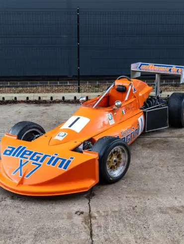 March 773 Formel-3-Rennwagen in Orange mit Allegri-Beklebung, Baujahr 1977, stehend auf einem Betonboden vor einem Zaun.