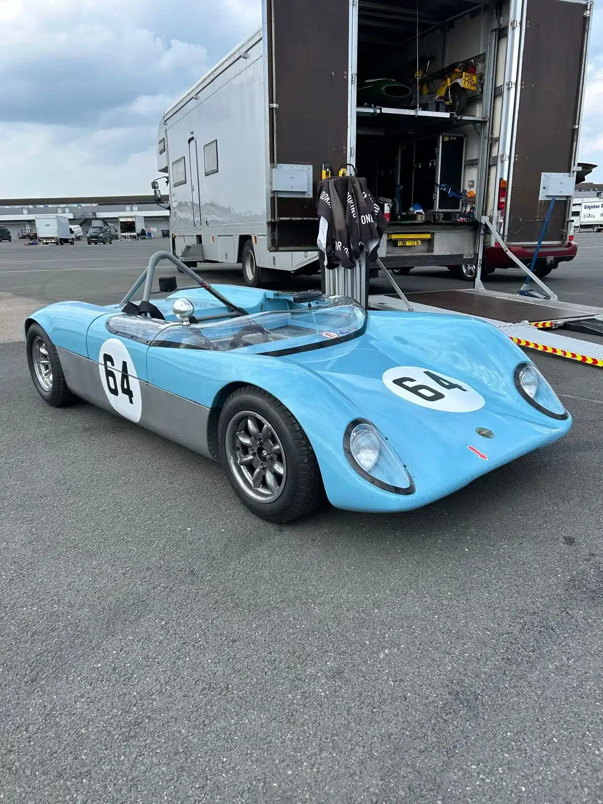 Merlyn Mk4A Baujahr 1964, hellblau mit Startnummer 64, steht bereit vor einem Transporter auf einer Rennstrecke