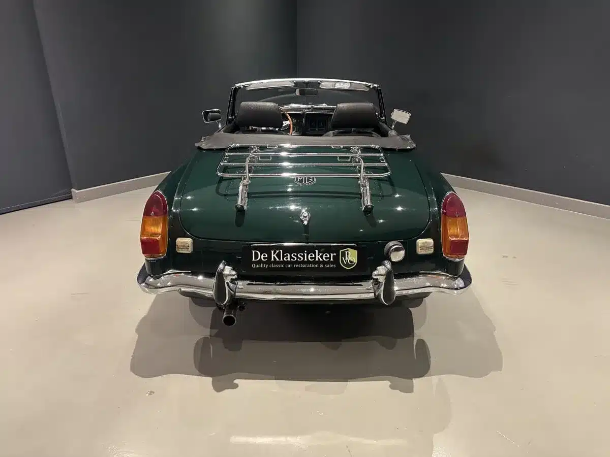 Heckansicht eines dunkelgrünen MGB MkIII Roadster mit verchromtem Gepäckträger und geöffnetem Verdeck.