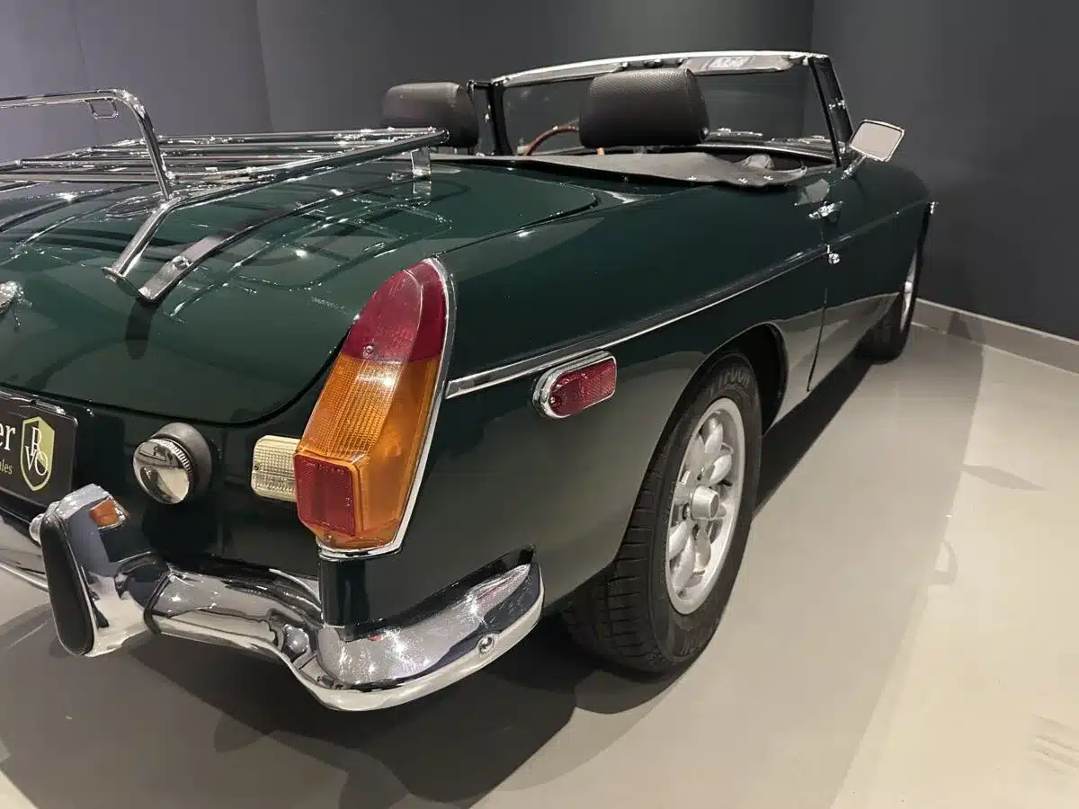 Heckansicht eines dunkelgrünen MGB MkIII Roadster von 1974 mit Chromstoßstange und verchromtem Gepäckträger.