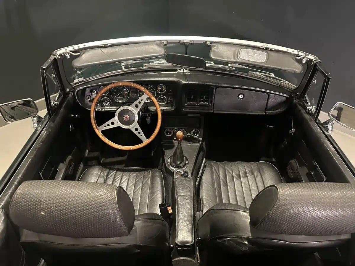Innenansicht eines MGB MkIII Roadster von 1974 mit originalem schwarzen Lederinterieur und Holzlenkrad.