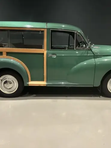 Grüner Morris Minor 1000 Traveller von 1964 mit sichtbarem Holzrahmen, im Ausstellungsraum seitlich fotografiert