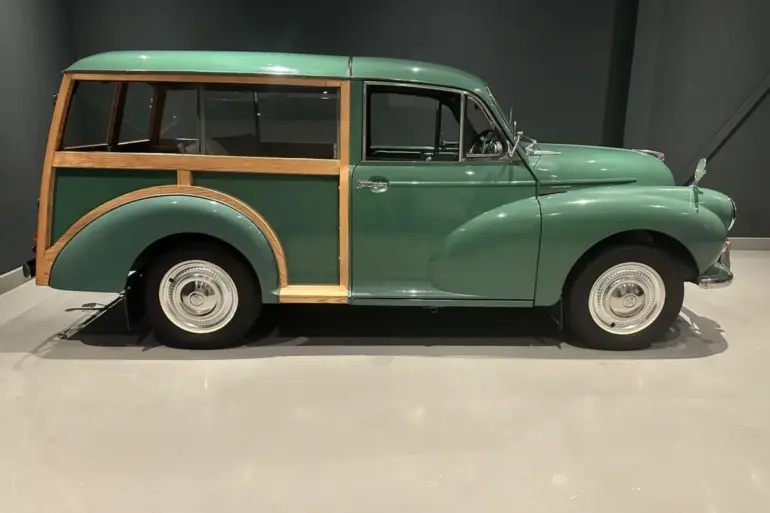 Grüner Morris Minor 1000 Traveller von 1964 mit sichtbarem Holzrahmen, im Ausstellungsraum seitlich fotografiert