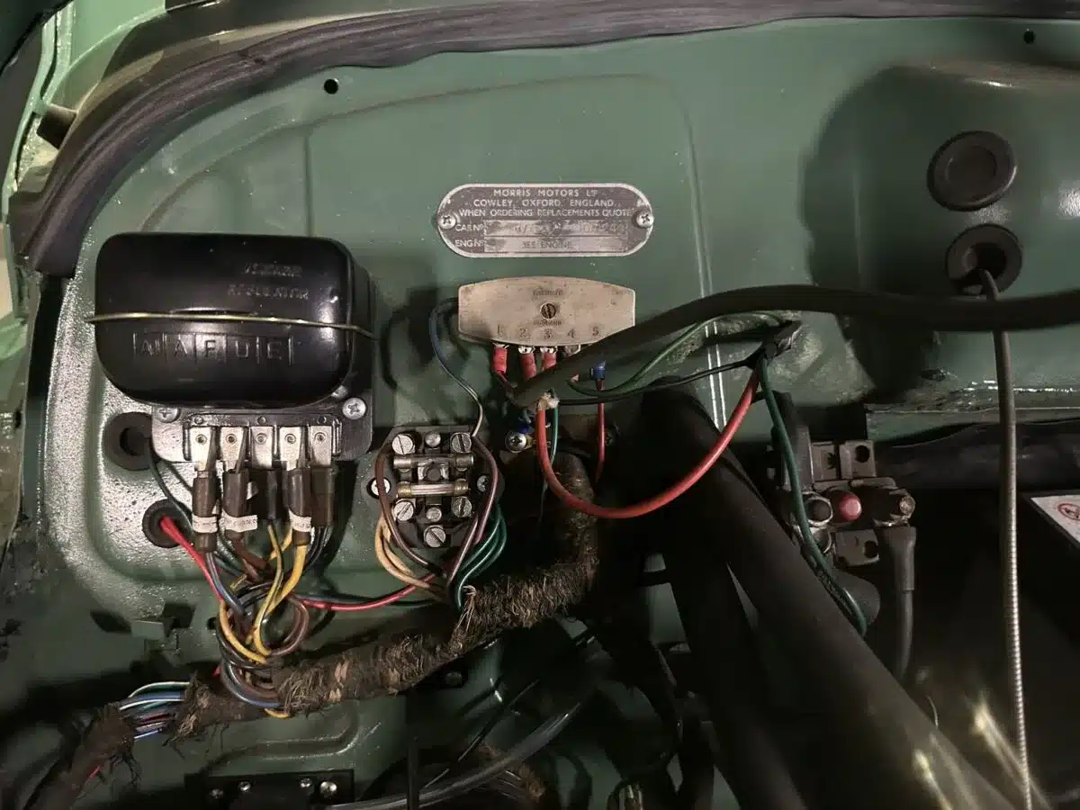 Elektrische Komponenten und Typenschild im Motorraum eines Morris Minor 1000 Traveller aus dem Jahr 1964.