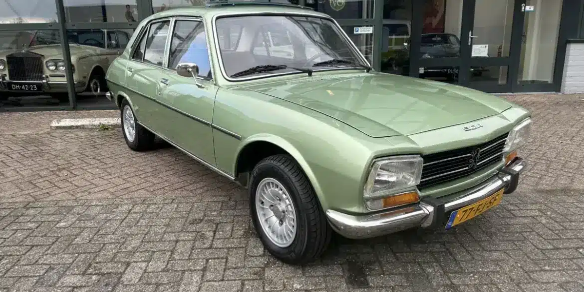 Grüner Peugeot 504 Ti aus den 1970er Jahren vor einem Autohaus, gut erhalten und fahrbereit.