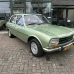 Grüner Peugeot 504 Ti aus den 1970er Jahren vor einem Autohaus, gut erhalten und fahrbereit.