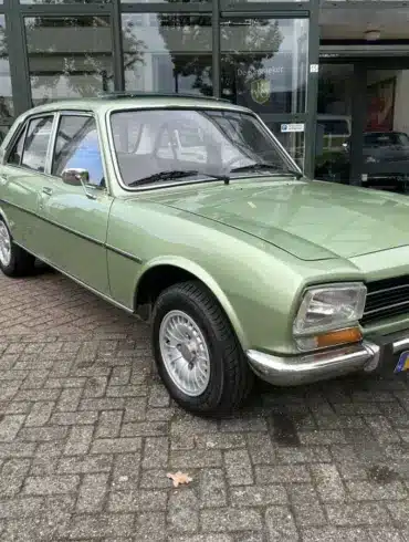 Grüner Peugeot 504 Ti aus den 1970er Jahren vor einem Autohaus, gut erhalten und fahrbereit.