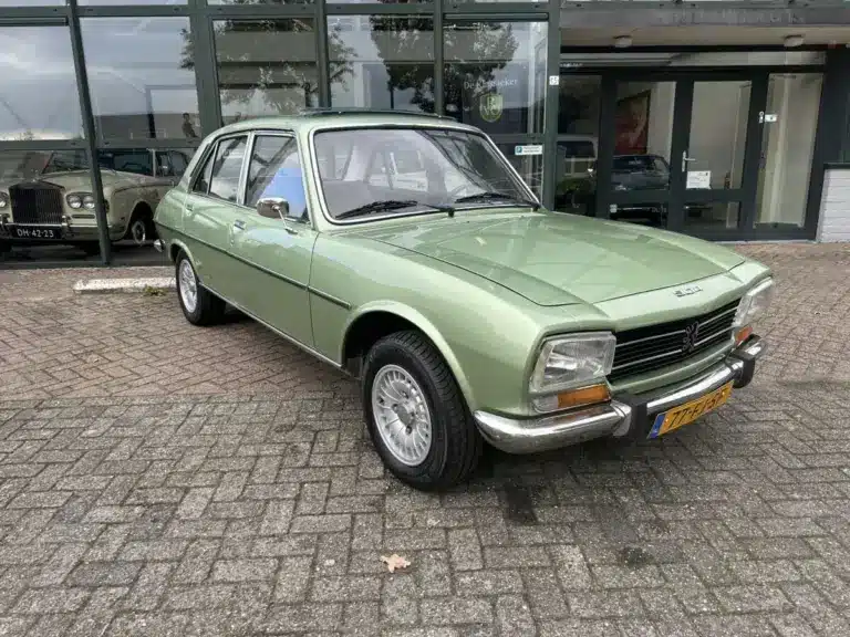 Grüner Peugeot 504 Ti aus den 1970er Jahren vor einem Autohaus, gut erhalten und fahrbereit.