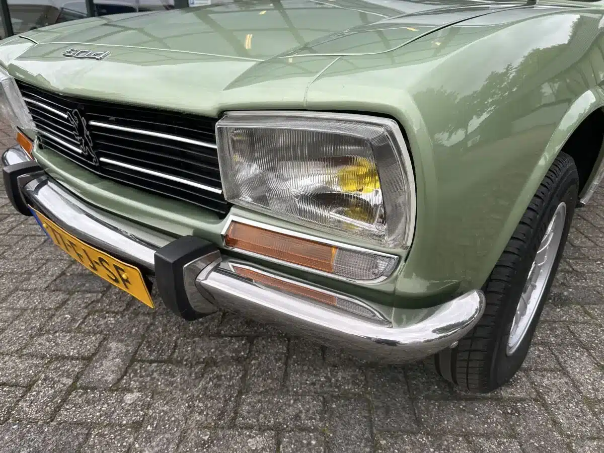 Nahaufnahme der Front eines Peugeot 504 Ti in grünem Lack vor einem Gebäude.
