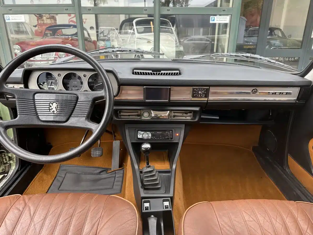 Blick auf das Cockpit und Armaturenbrett eines Peugeot 504 Ti mit braunen Sitzen, Lenkrad und Anzeigen.