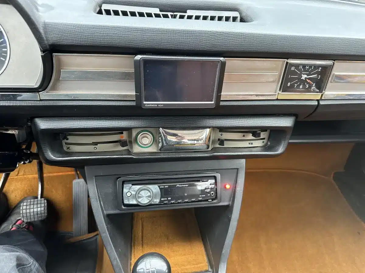 Zentralansicht auf Armaturenbrett und Mittelkonsole eines Peugeot 504 Ti, mit Uhr, Lüftung, Navi und Nachrüstradio