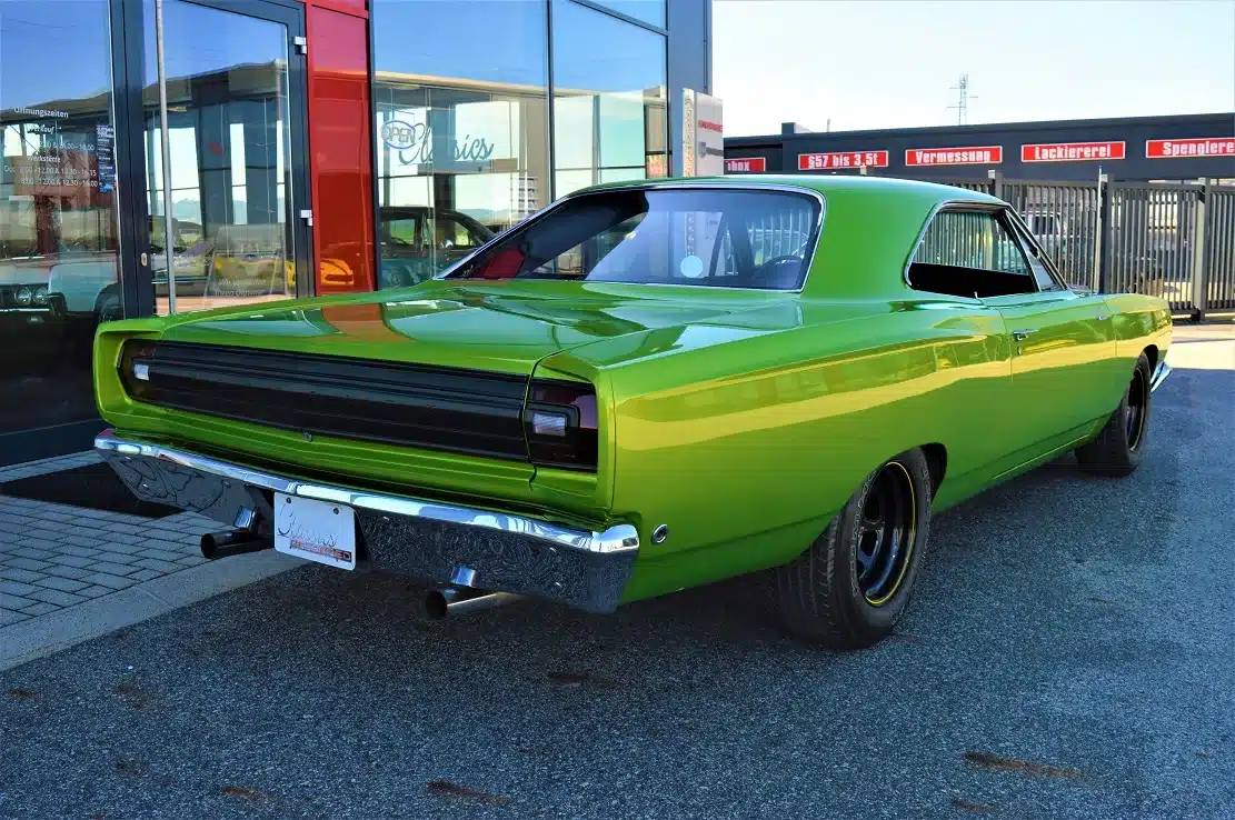 Grüner Plymouth Road Runner 383 von 1968, fotografiert von hinten auf einem Parkplatz vor modernen Glasfassaden