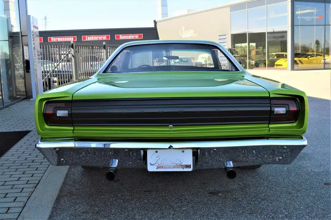 Heckansicht eines grünen Plymouth Road Runner 383 von 1968 mit zwei Auspuffrohren vor einem Autohaus.