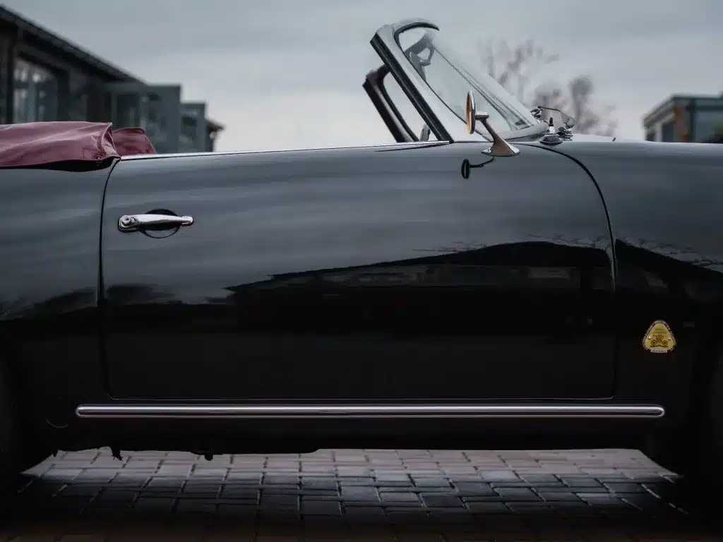 Nahaufnahme der Seitenansicht eines schwarzen Porsche 356 B Roadster mit offenem Dach und rotem Interieur