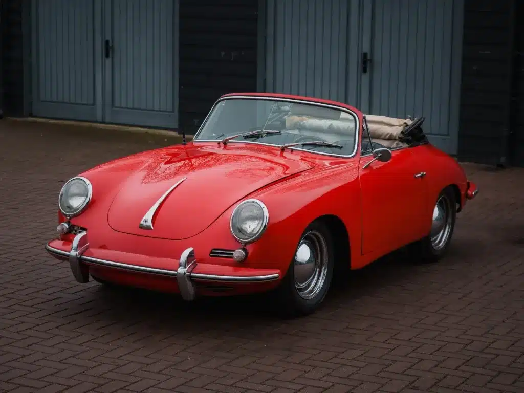Porsche 356 C Cabriolet von 1965 in roter Lackierung mit offenem Verdeck, stehend vor einer Garage