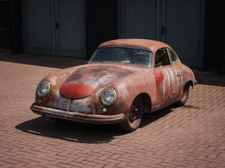 Porsche 356 Pre-A Coupé 1952 in unrestauriertem Zustand mit sichtbar gealtertem Lack und Korrosionsspuren, abgestellt auf Pflastersteinen vor einer Garage.