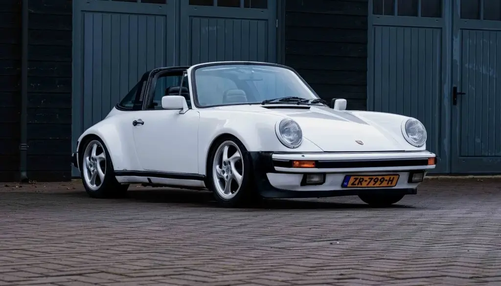 Weißer Porsche 911 3.2 Targa aus dem Baujahr 1984 mit niederländischem Kennzeichen, geparkt vor einer dunklen Garage