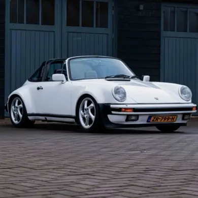 Weißer Porsche 911 3.2 Targa aus dem Baujahr 1984 mit niederländischem Kennzeichen, geparkt vor einer dunklen Garage