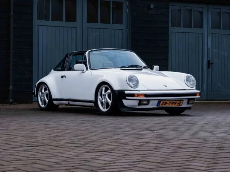 Weißer Porsche 911 3.2 Targa aus dem Baujahr 1984 mit niederländischem Kennzeichen, geparkt vor einer dunklen Garage