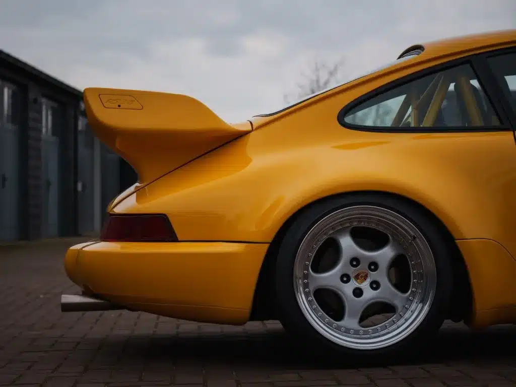 Detailansicht des gelben Porsche 911 SC mit 964 RS Heckflügel und Speedline-Felge, aufgenommen von schräg hinten.